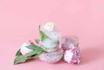 peonies flowers frozen in ice on a pink background, creative summer concept