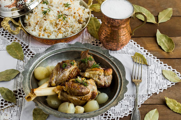 Lamb shank,rice and buttermilk drink,served on wooden table with handmade lace tablecloth and old vintage copper dishes.Traditional Islamic Feast or any holiday concept.