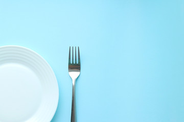 An empty flat white plate and a metal fork on a blue background. The view from the top. Space for text. Selective focus. Serving. Copy space