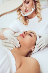 Obraz na płótnie Canvas Beautiful and attractive adult woman receiving professional facial care beauty treatment with peeling mask.