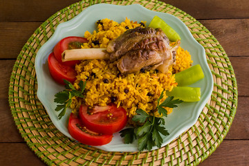 Traditional Arabic yellow rice with tomato,pepper,parsley and lamb shank in the round plate,whicker pad under of it.The Sacrifice Feast Concept