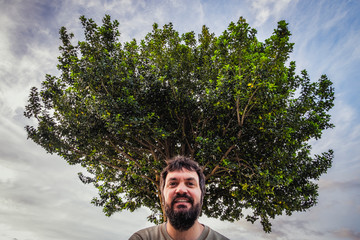 Homem sorridente com barba e grande árvore a trás