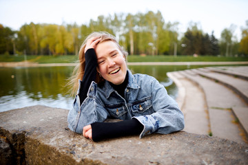 Beautiful close-up portrait of a red-haired teenage girl in 90's jeans in a park near a lake