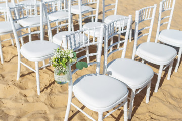 Wedding ceremony on the beach. A set of white chairs for guests decorated with flowers.