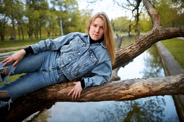 Redhead teen hippie girl authenticly lies on a tree above the water in the park