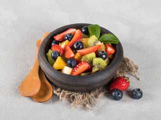 Fruit berry salad of strawberries, orange, Apple, kiwi, blueberries in a wooden bowl on a linen napkin on a light background in rustic style
