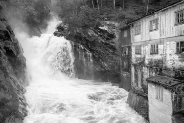 Old power plant next to powerful white watered waterfall in Otta city in Norway.