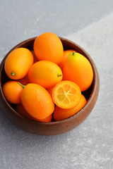Bowl full of fresh kumquat fruit on grey concrete background.