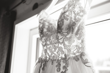 Black and white close up of beautiful lace at wedding dress hanging at window. Back-light photo. Wedding day concept.