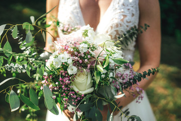 Colorful flowers in wedding bouquet against bride in white wedding gown. Outdoor background....