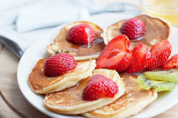 Breakfast with pancakes with strawberry, kiwi and honey on white background. Tasty breakfast for child on wooden board