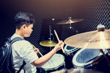 Asian man put black t-shirt to playing the drum set with wooden drumsticks in music room , the...