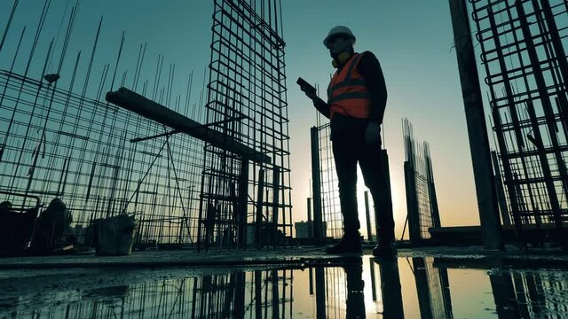 Builder checks his phone while standing on construction site.