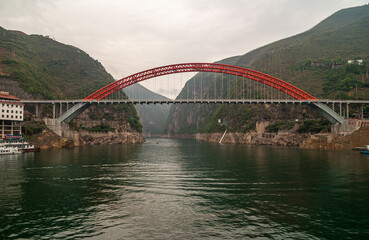 Wushan, Chongqing, China - May 7, 2010: Wu Gorge in Yangtze River. Red S103 road bow bridge over Daning River at connection with green Yangtze. Green mountains under silver sky.