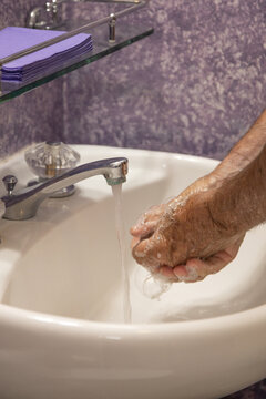 Man soaping hands in bathroom sink with running water from faucet