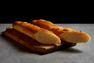 
Halved fresh baguette on a wooden board. Black background.