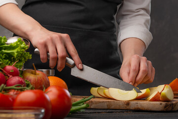 Chef cuts vegetables and fruits, apples for cooking. Against the background of a gray wall. Delicious and culinary recipes.
