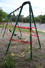 Fototapeta na wymiar Danger tape is wrapped around playground equipment, indicating the park is closed due to Covid-19 concerns.