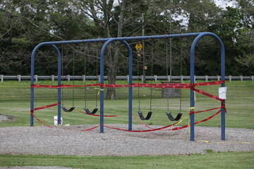 Fototapeta na wymiar Danger tape is wrapped around playground equipment, indicating the park is closed due to Covid-19 concerns.