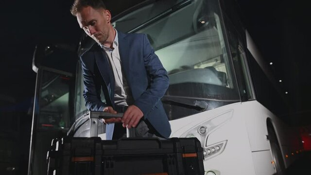 Caucasian International Travel Coach Bus Driver in His 30s with His Equipment Preparing For the Next Trip. Public Transportation Industry.