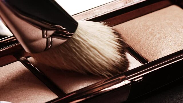 Big lush brush gains powder, bronzer and highlighter on pile to be used in make-up. Artist working with face palette. Details of working process, tools in beauty industry. Decorative cosmetics.
