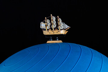 Small wooden boat over a blue giant fit ball and a black background. Travel and adventure concept photography