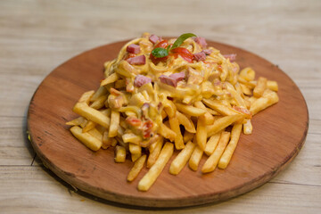 Patatas fritas con queso cheddar y panceta sobre tabla de madera redonda en una mesa de madera.