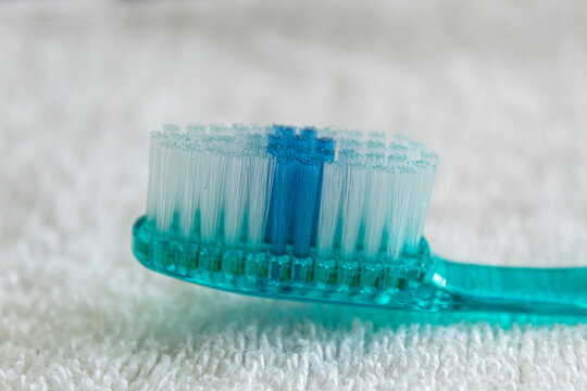 Closeup to a blue thooth brush with white tufts and blue head over a  white towel background.