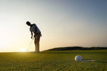 Golf ball that is about to falling in last hole along with blurred golfers as a background amid the...