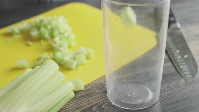 a woman prepares slices on a cutting board ingredients for a celery smoothie and puts them in a blender bowl