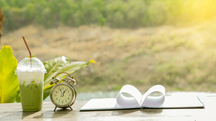 Stop for a cool green tea with a clock and heart-shaped notebook on the coffee shop table with a blurred background.