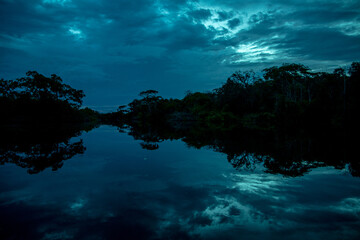 Blue Dark Dramatic River at Sunset with a Perfect Reflection of the Trees and Clouds on the Water
