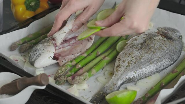 fresh gutted and seasoned with salt and salt ready to bake dorado fish on a baking sheet covered with baking paper with asparagus, lime, young garlic and onions.