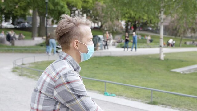 A young man with a mask taking a break during coronavirus. People walking in the background.