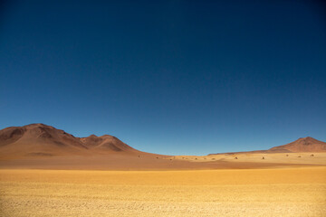 Fototapeta na wymiar Salvador Dali desert on a Clear Blue Sky Day with Dream Like Yellow Sand and Mountain Ranges near Uyuni Salt Flat