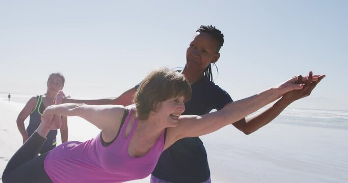 African American yoga teacher woman helping woman on the beach and blue sky background