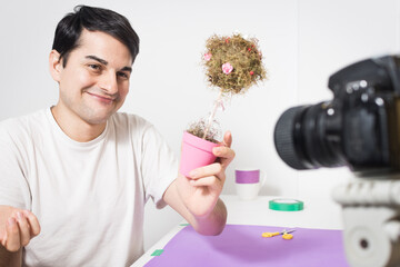 Young male making a handmade souvenir. Man doing a tree, Filming live video vlog. Smiling to the camera, Social media influence people. Working at home. Educational videos for children.