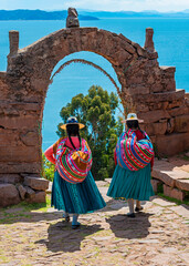 Two Peruvian Quechua indigenous women in traditional clothes walking through the arch of the rulers...