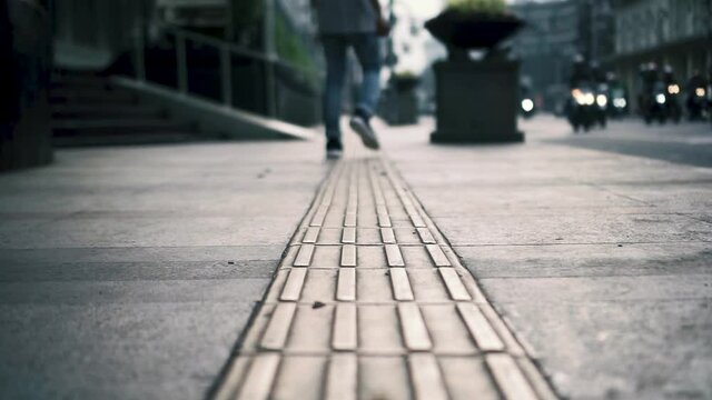 Low angle shot of man walking away, busy street, tactile tiles for blind people