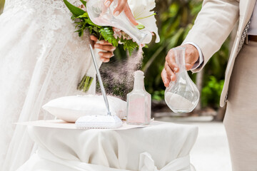 Bride and groom pouring colorful different colored sands into the crystal vase close up during symbolic nautical decor destination wedding marriage unity ceremony on sandy beach in front of the ocean 