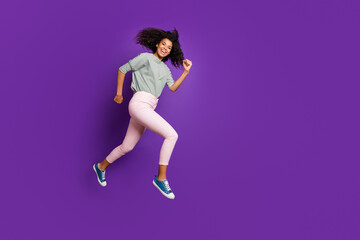 Fototapeta na wymiar Full body photo of cheerful afro american girl jump run hurry fast after black friday discounts wear casual style outfit pants isolated over violet color background