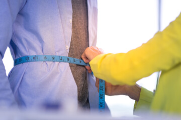 A female tailor is measuring the waist of a male client with a tape measure