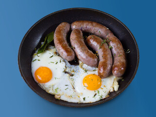 Homemade delicious sausages and fried eggs in a pan on a wooden surface. Side view