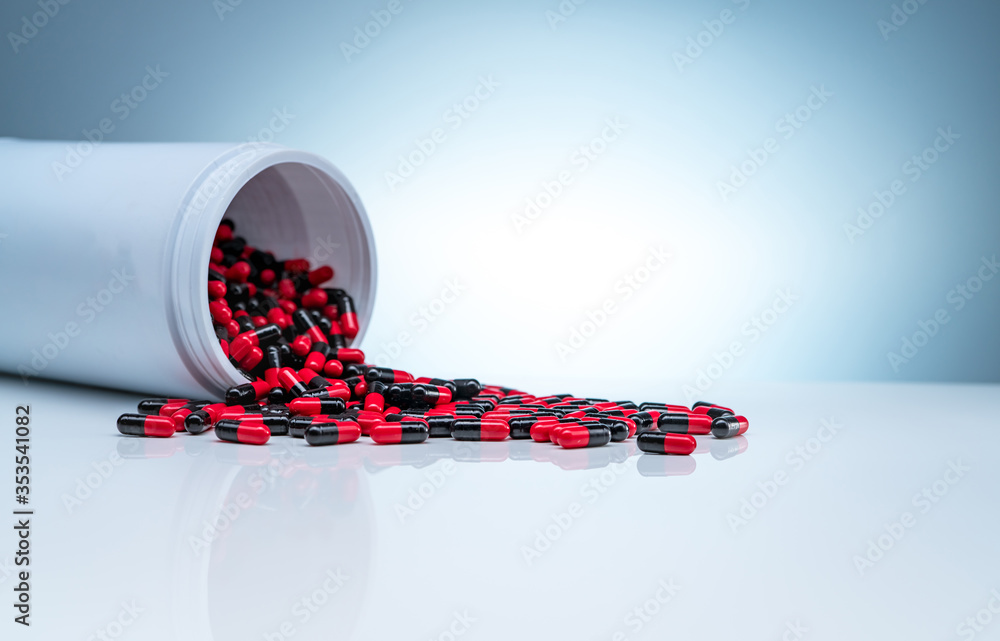 Wall mural Red-black antibiotic capsule pills spread out of white plastic drug bottle on gradient background. Pharmaceutical industry. Antibiotic drug resistance concept. Healthcare and pharmaceutics concept.