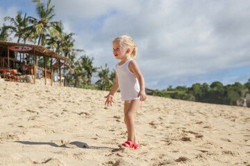 Little toddler girl enjoying a hot summer day at the tropical sandy beach