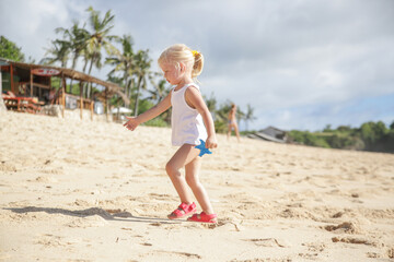 Little toddler girl enjoying a hot summer day at the tropical sandy beach