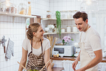 Happy & smiling attractive young cute caucasian couple in love enjoying cooking healthy salad in kitchen at home together. Happiness family of beautiful romantic married lover or marriage relationship