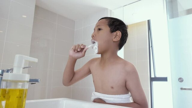 Young Asian boy brushing his teeth in bathroom, messy face, foaming toothpaste