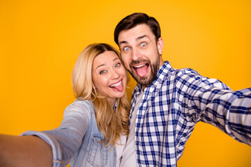 Closeup photo of blond lady handsome guy funky couple spend quarantine together making selfies fooling around stick tongue out mouth wear casual shirts isolated yellow color background