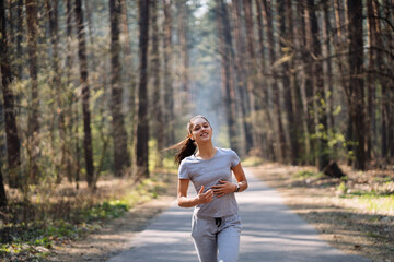 Beautiful young woman running in green park on sunny summer day